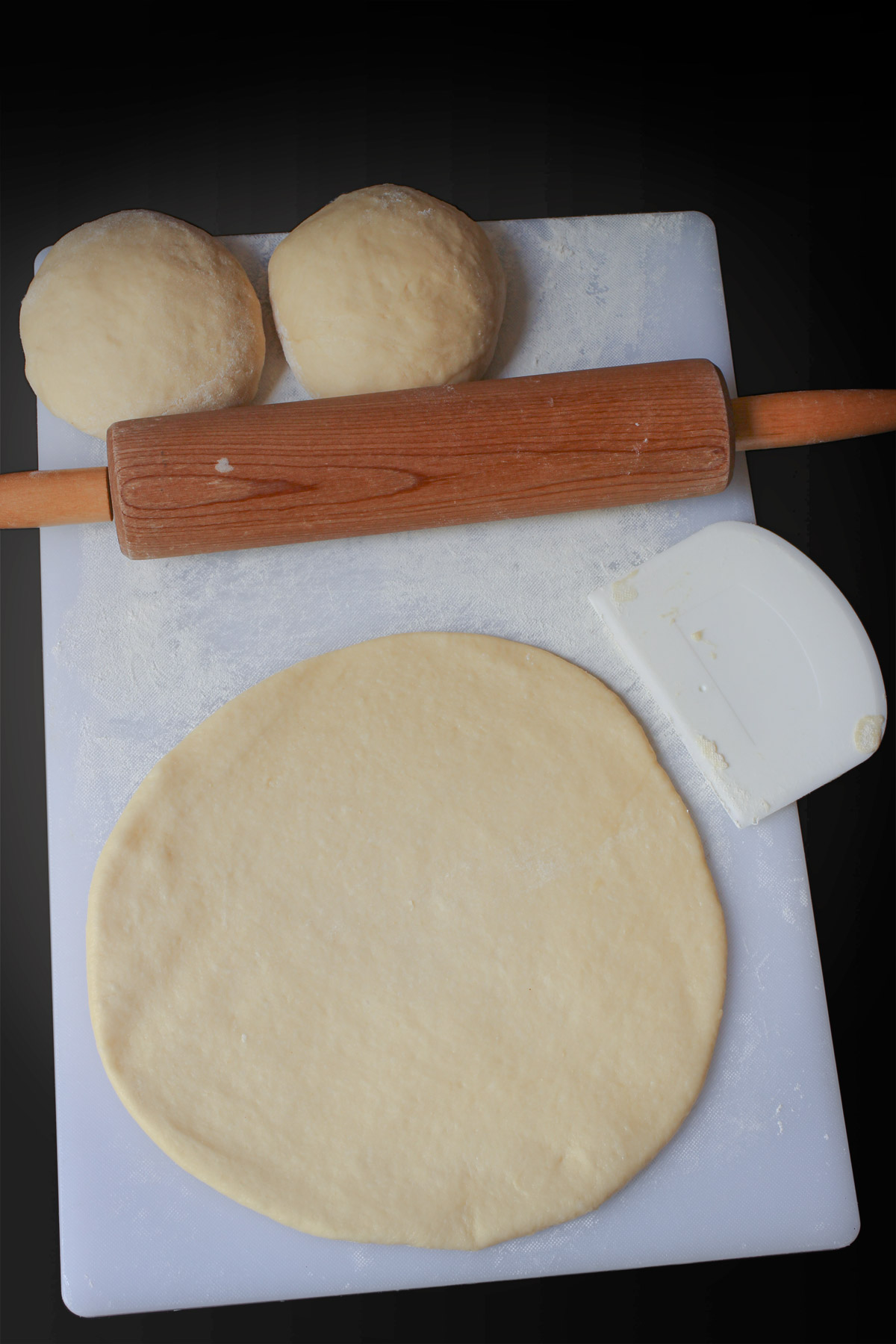 the round of dough on the floured surface with a bench knife, rolling pin, and two more balls of dough.