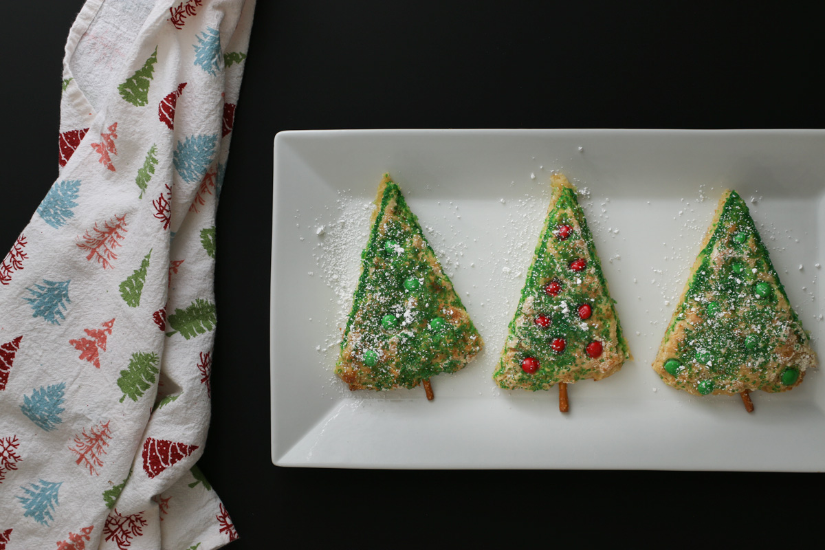 three christmas tree scones on a white rectangular platter with a christmas tree towel nearby.
