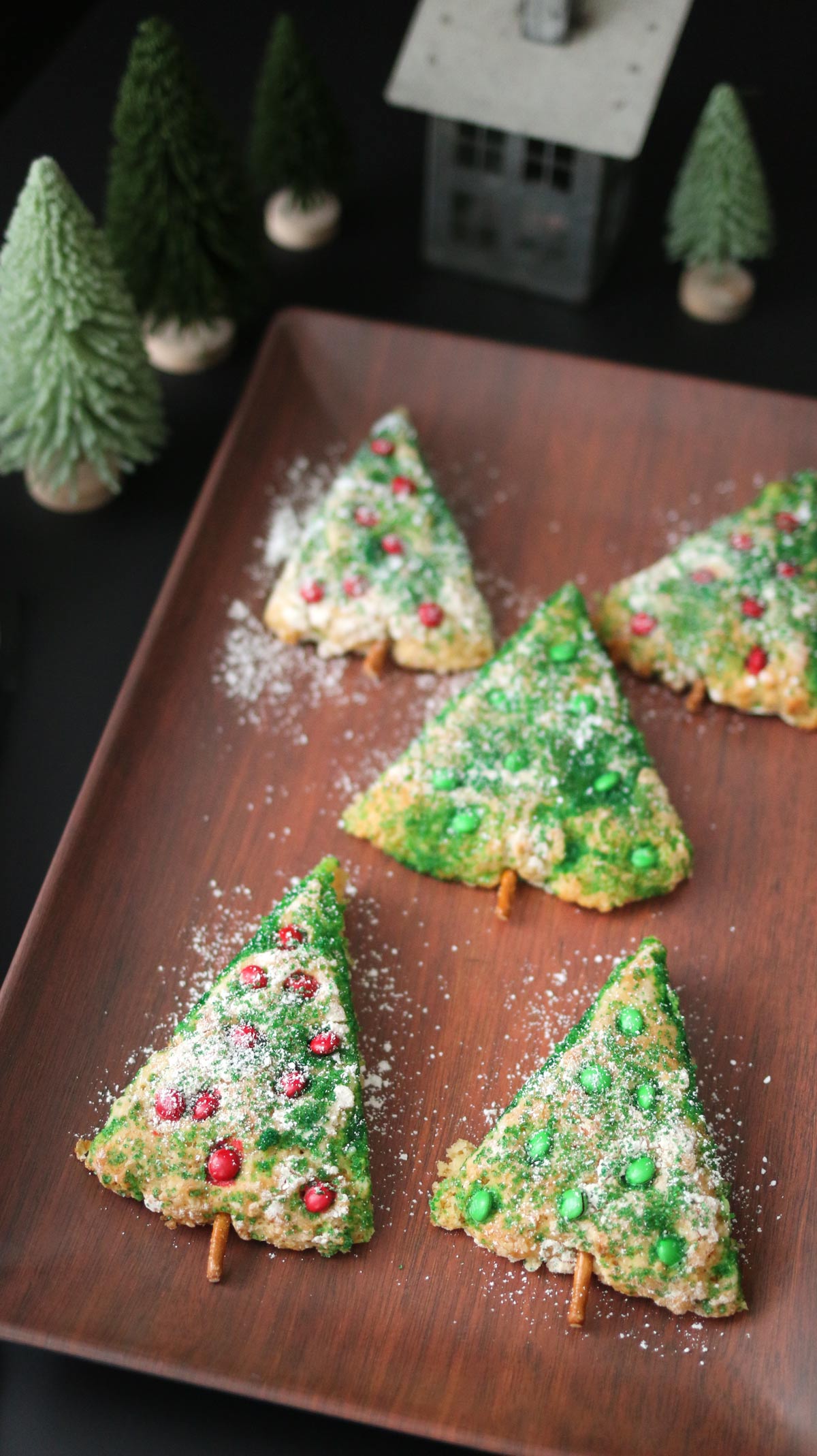 five christmas tree scones on a wooden platter with christmas village decor nearby.