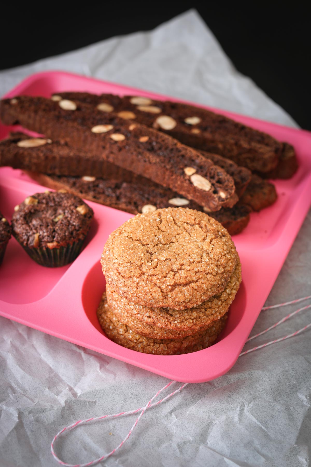 pink divided tray containing chocolate almond biscotti, molasses crinkles, and brownie bites.