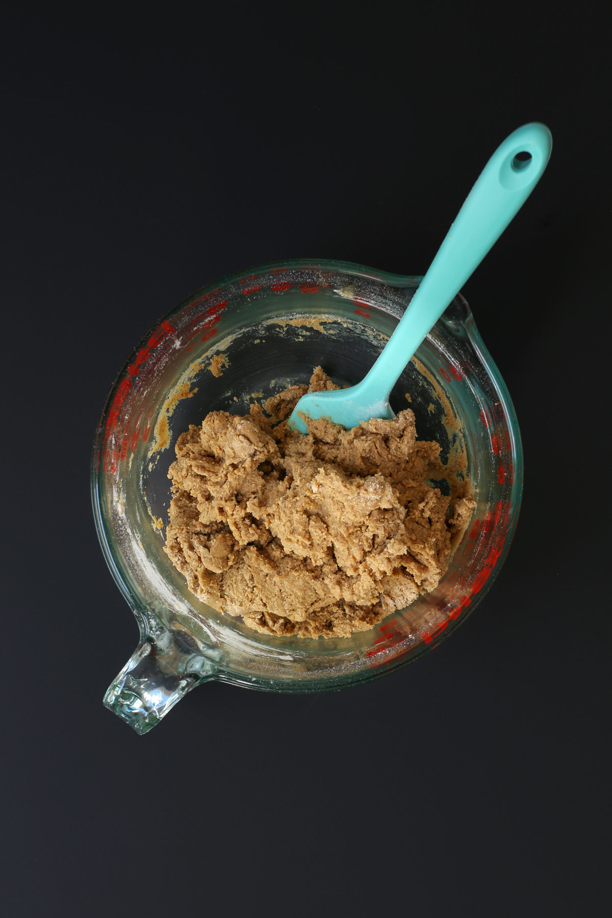 a teal rubber spatula immersed in the molasses cookie dough in the pyrex bowl.
