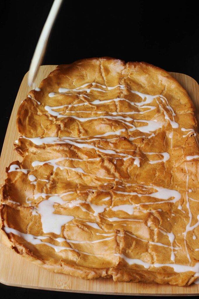 drizzling glaze off the wooden spoon onto the baked kringle pastry.