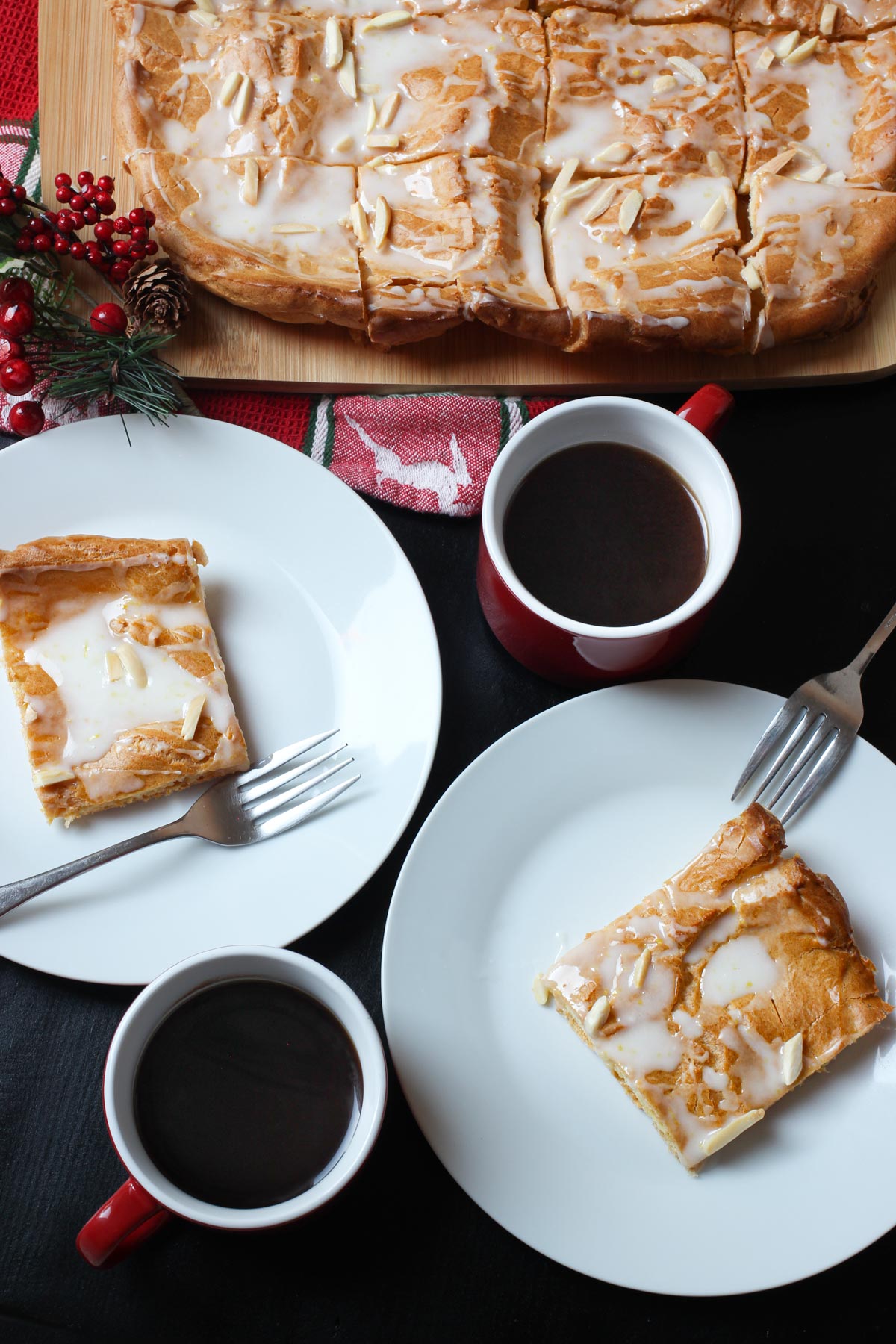 large kringle cut into squares and dished up on plates with cups of coffee nearby.