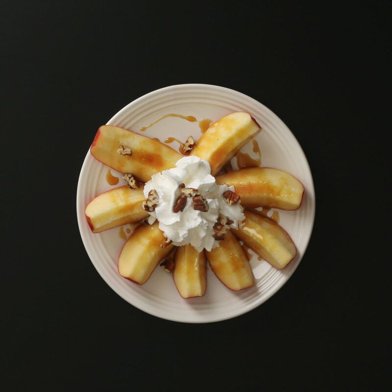 apple slices in crown shape on plate with whipped cream and nuts atop them.