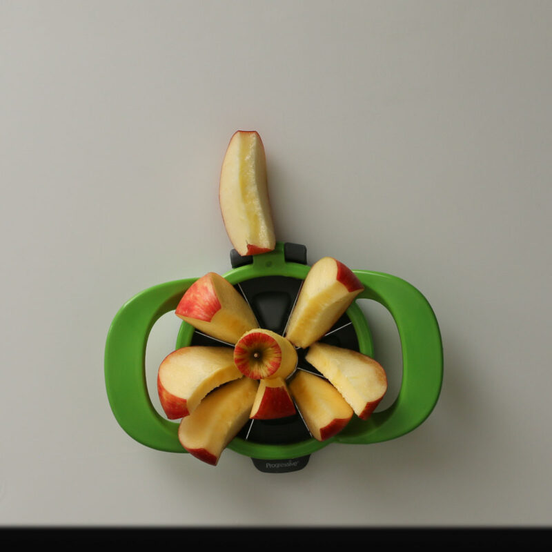 apple cut with green hand-held apple slicer on white cutting board.