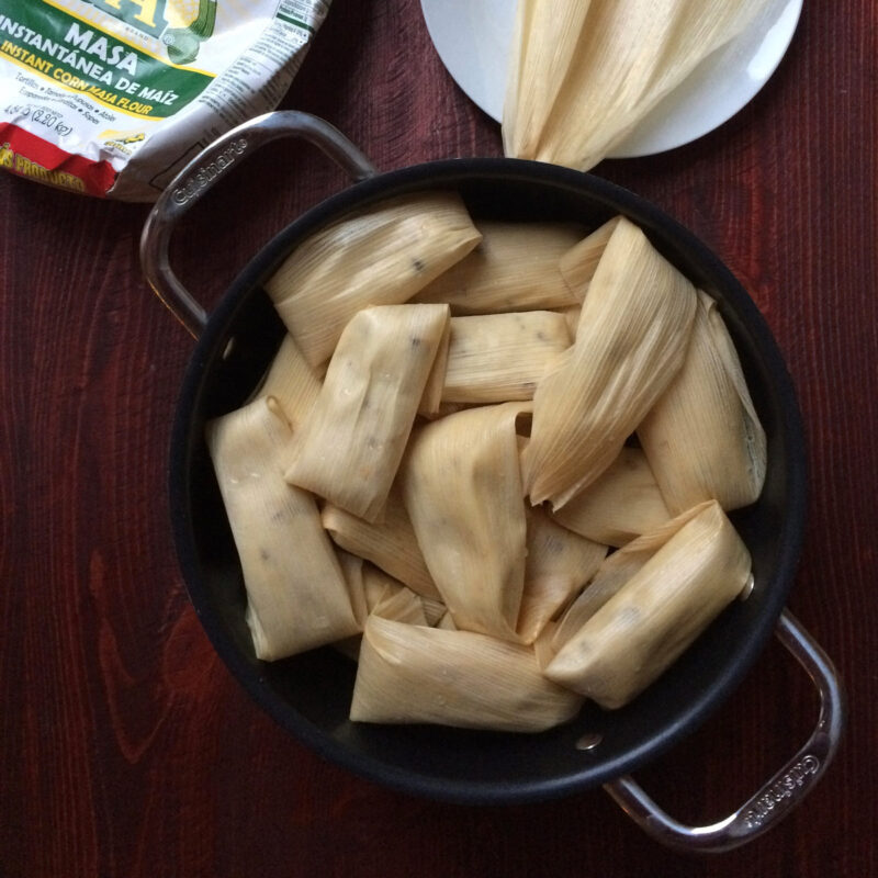 tamales ready to steam in a pot next to a cornhusk and bag of masa.