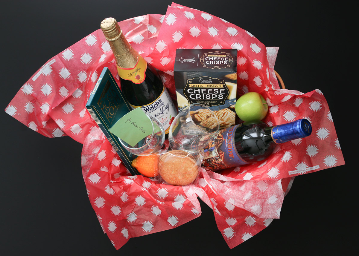 overhead shot of wine and cheese gift basket on a black table.
