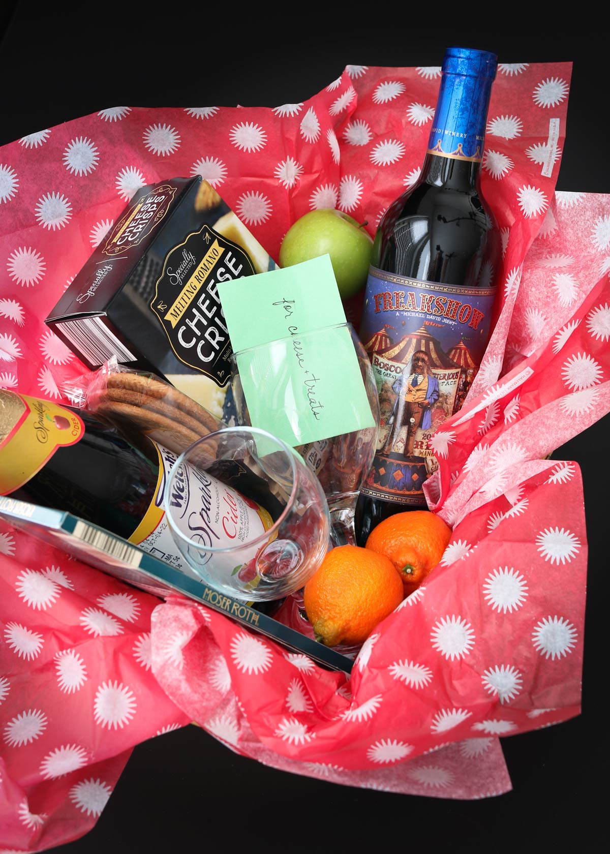 wine and cheese basket featuring wine, fruit, crackers, chocolate, cider, and a gift card for cheese.