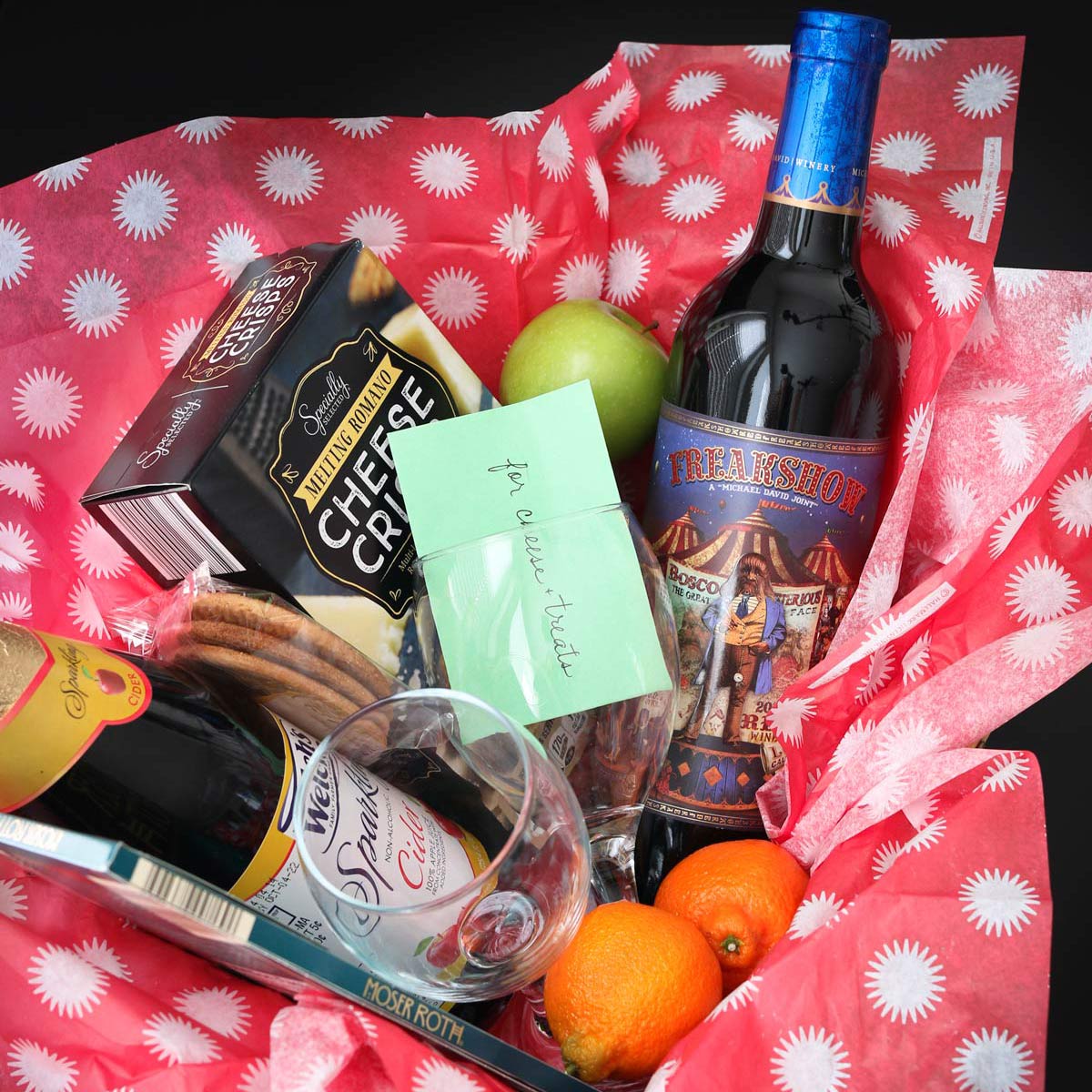 close up of wine and cheese gift basket lined with red tissue paper.