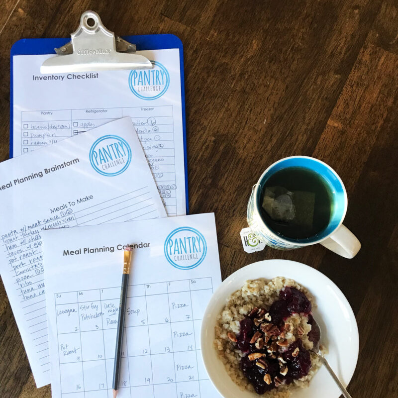 blue clipboard with planning worksheets near cup of tea and bowl of oatmeal.