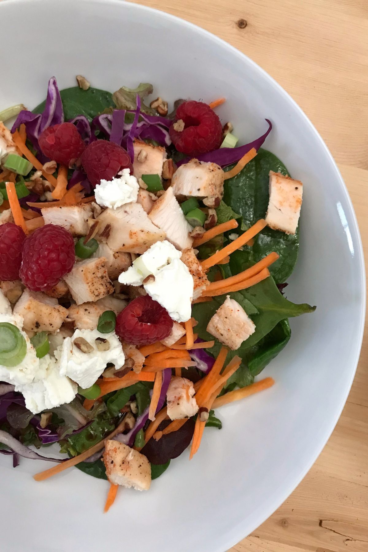 white bowl of salad with raspberries and cubed chicken.