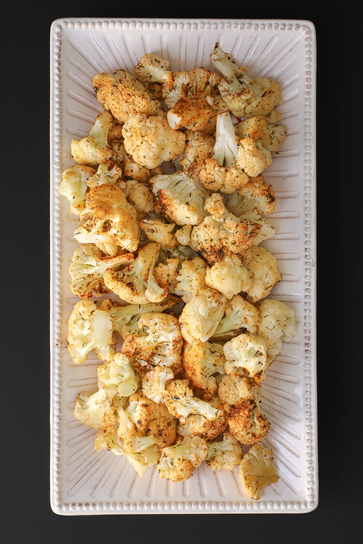 air fryer cauliflower on a white platter on a black table.