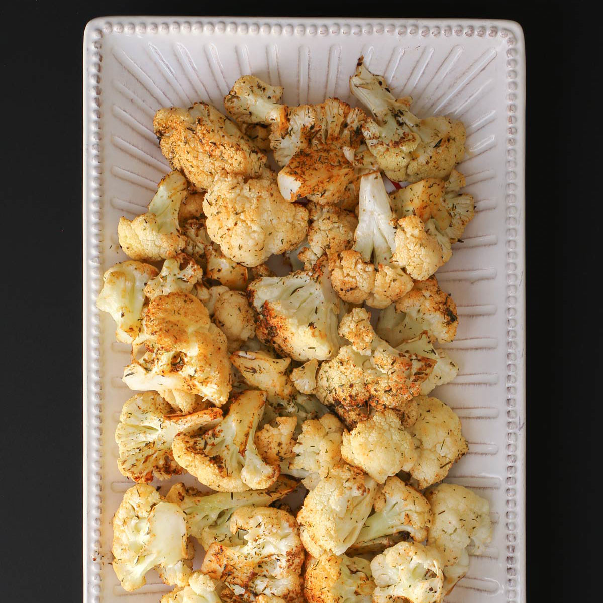 overhead shot of air fryer cauliflower on a white platter on a black table.