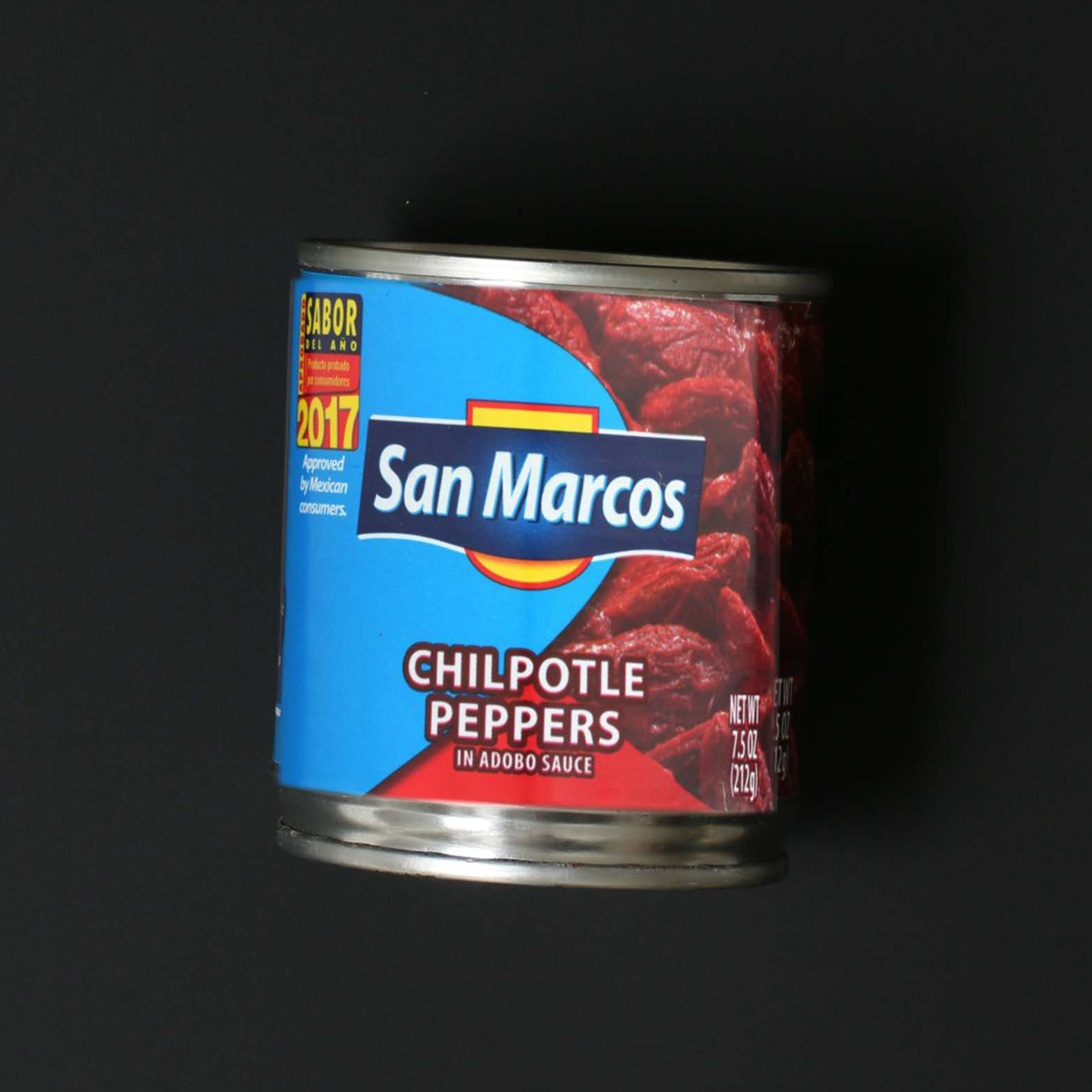 can of san marcos brand chilpotle peppers on its side on a black countertop.