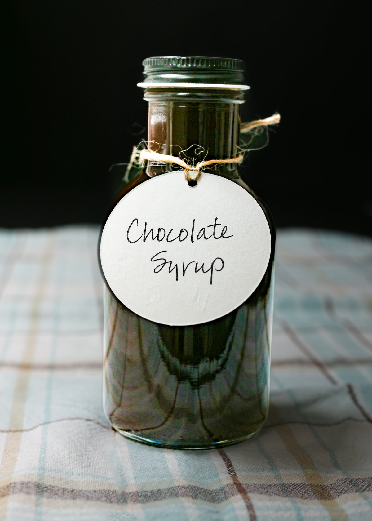 chocolate syrup in a glass bottle with a tag tied around the neck with twine, handprinted words on the tag read, "chocolate syrup".