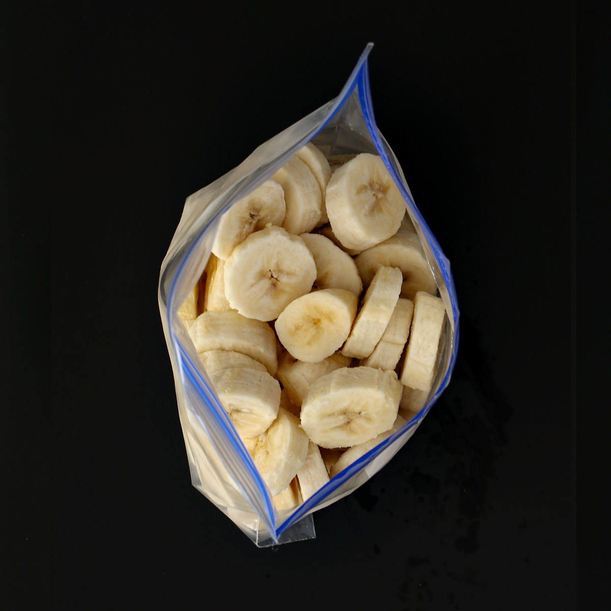 open freezer bag of frozen banana slices on black table top.