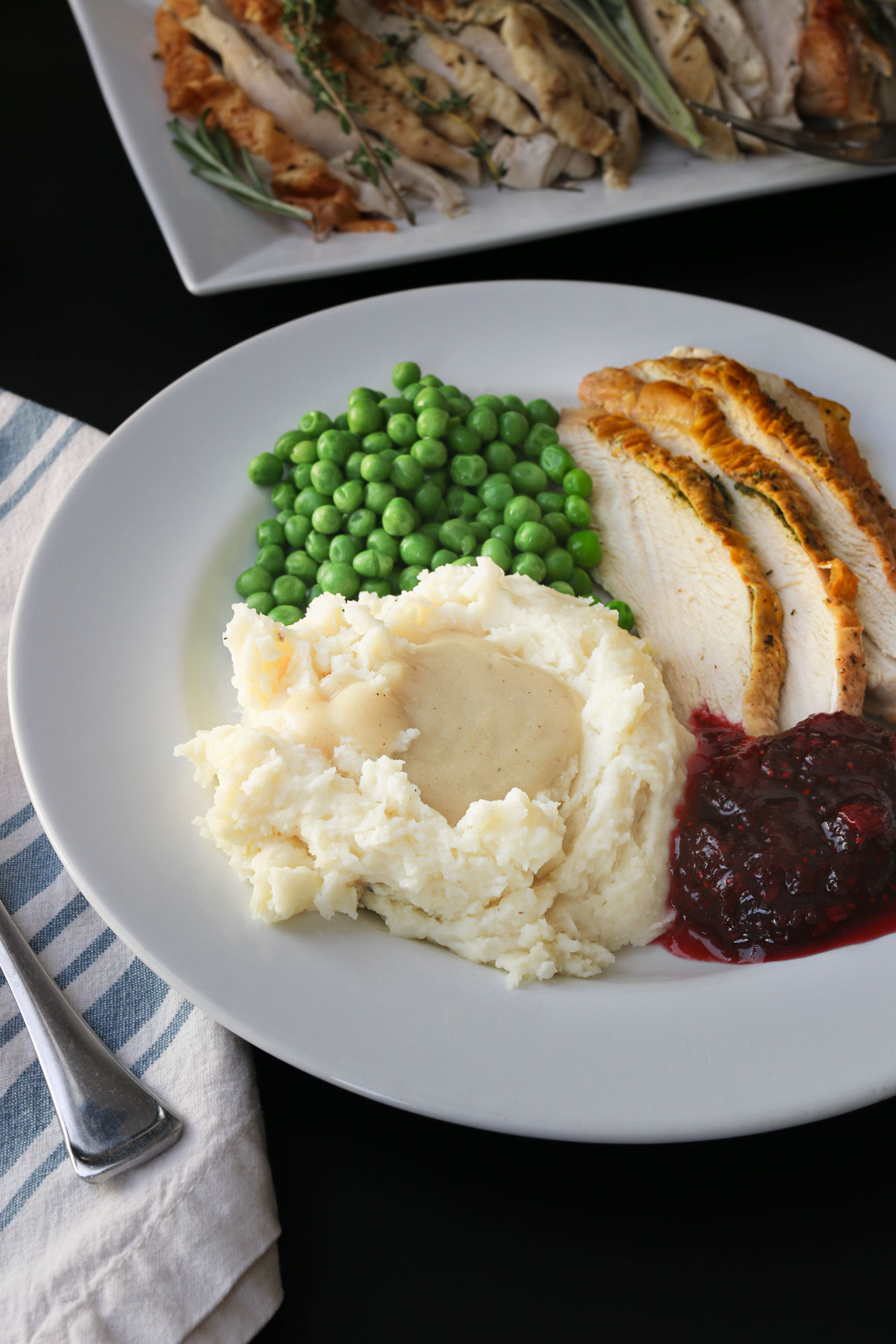 dinner plate with mashed potatoes, gravy, peas, roast turkey, and cranberry sauce.