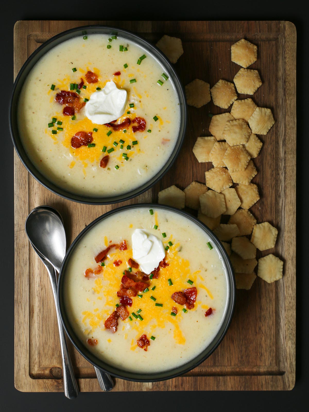 bowls of potato soup on a wood board with oyster crackers.