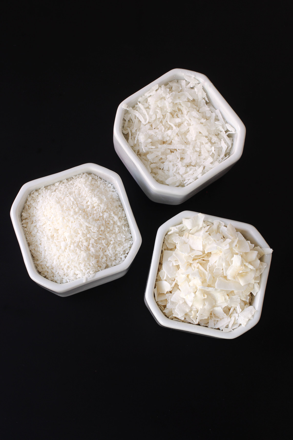 different size coconut shreds in white dishes on black table top.
