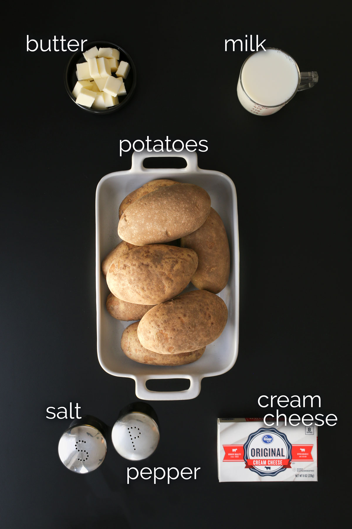 ingredients for mashed potatoes laid out on a black table top.