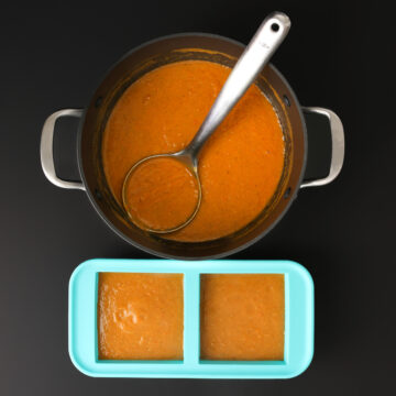 ladle immersed in finished soup in stock pot next to 2-cup soupercubes filled with soup.