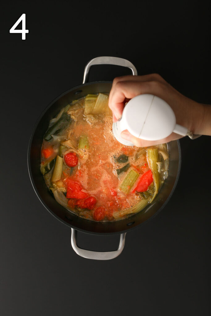immersion blender immersed in cooked vegetables in water.