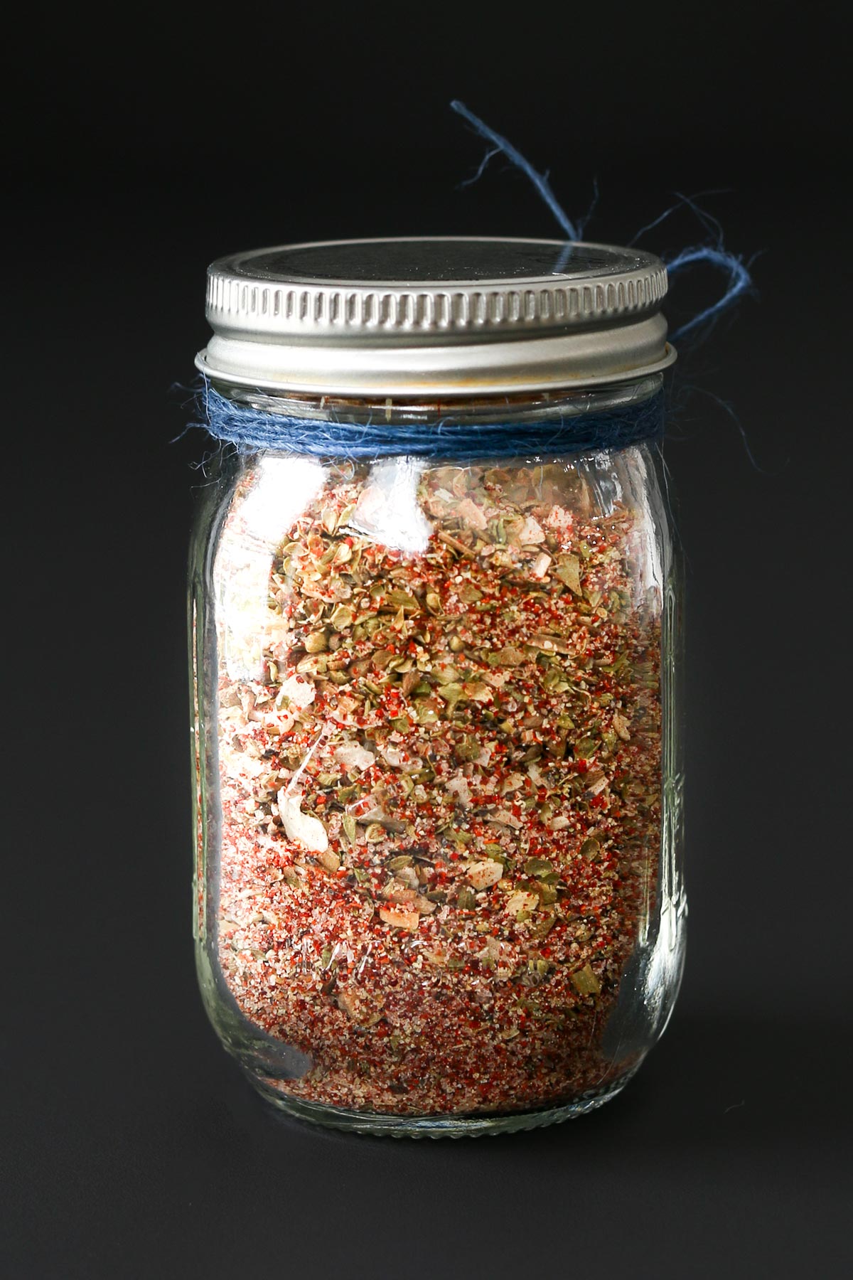 glass jar of taco seasoning mix tied with blue twine and topped with a metal lid.