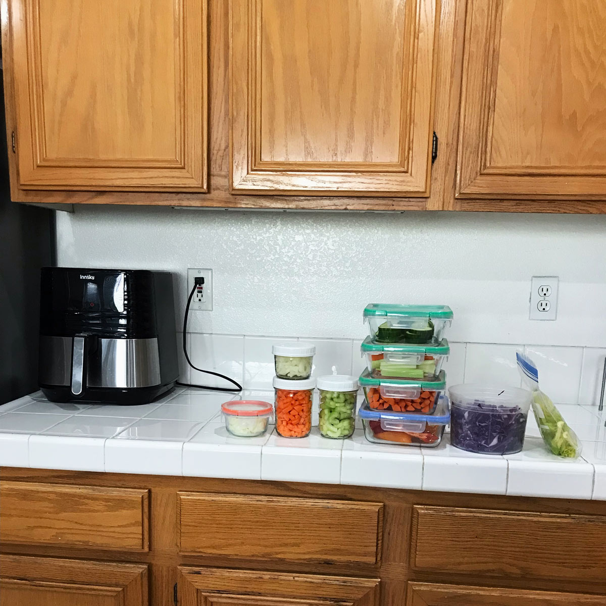 view of kitchen counter with air fryer and prepped veg in containers.