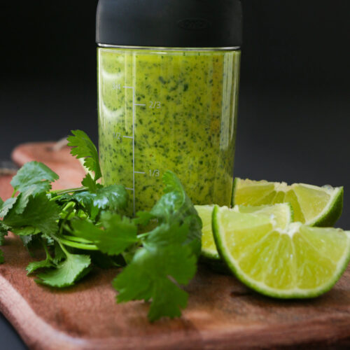 cilantro lime dressing in a carafe on a board with lime and cilantro.