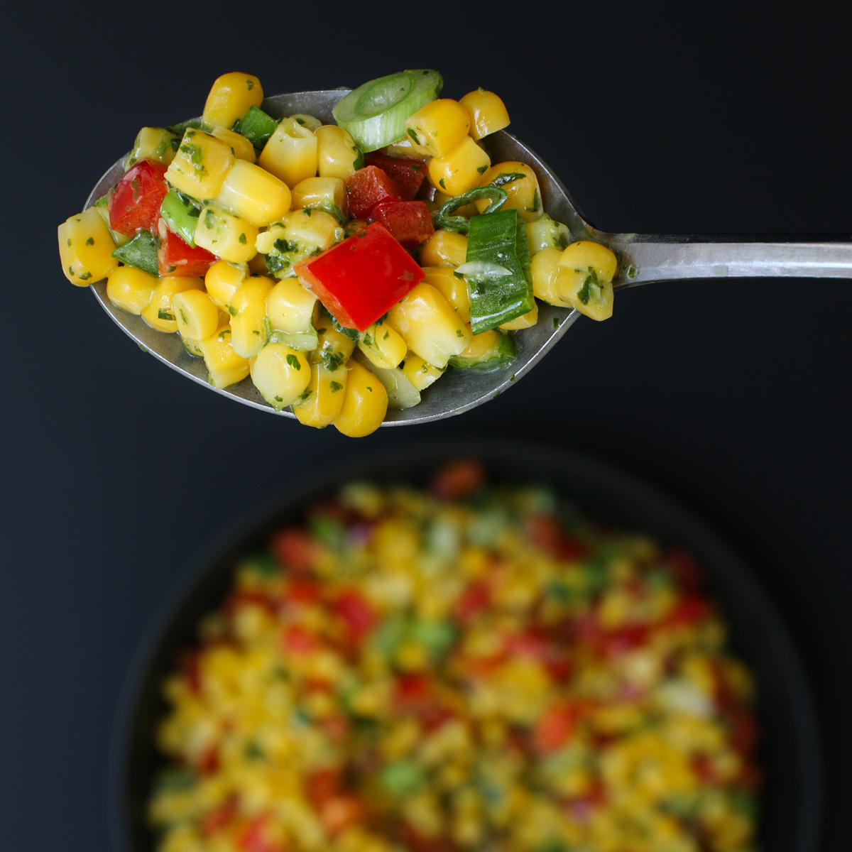 overhead shot of large spoonful of corn salad held above a bowl of salad.