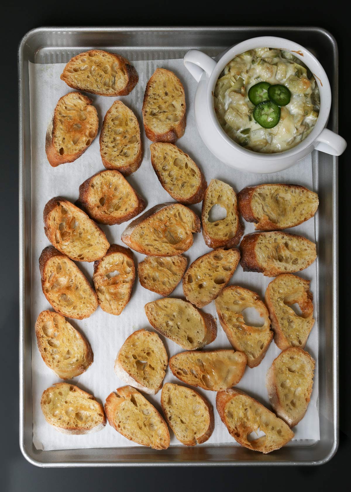 toasted baguette on sheet surrounding the baked dip, jalapeno slices have been added to the dip.
