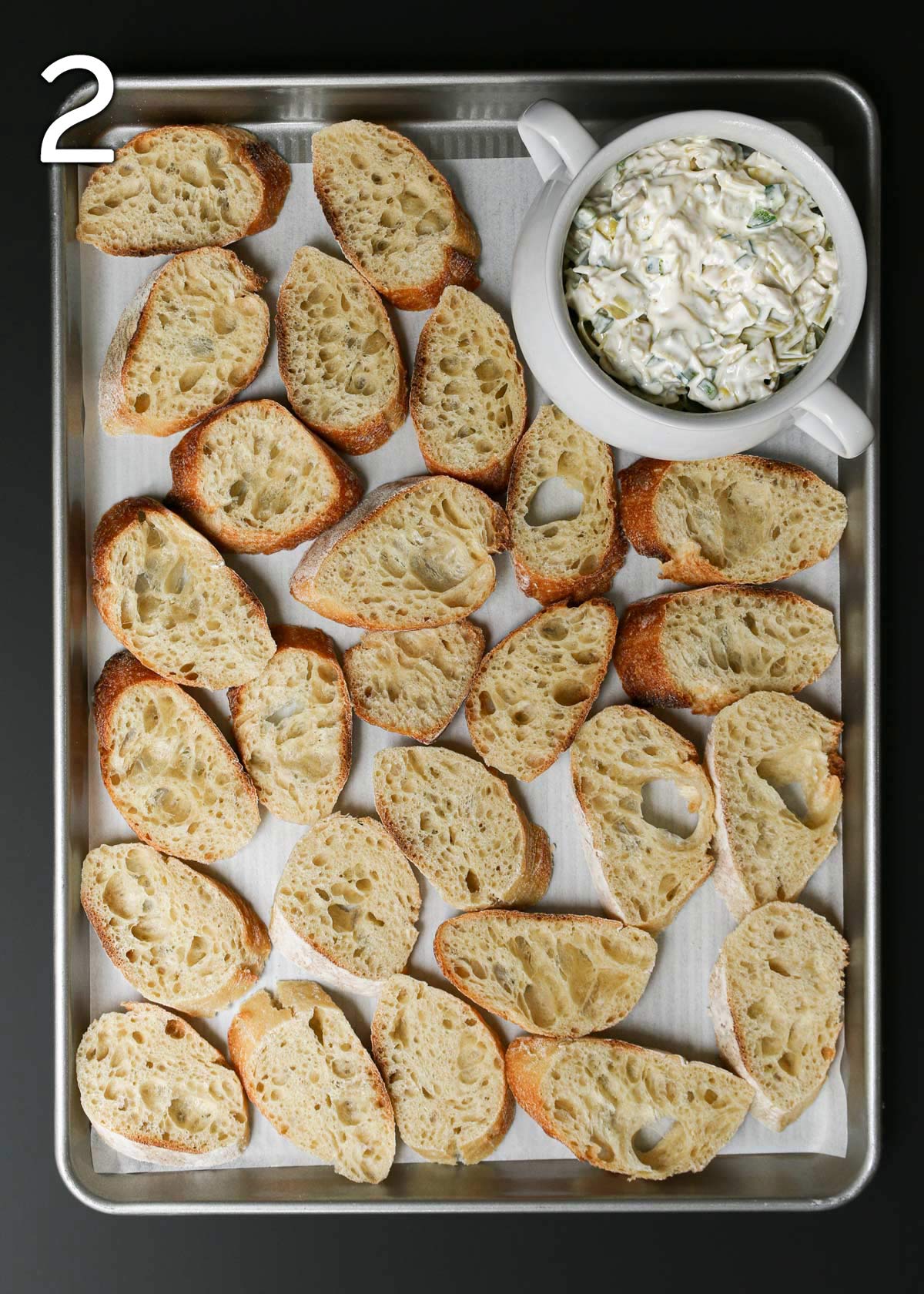 dip tureen on baking sheet with sliced baguette laid out around it.