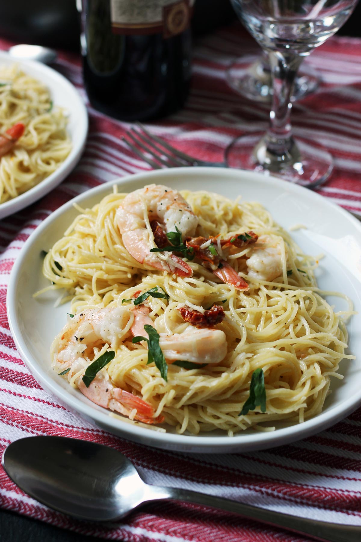 close up of a plate of shrimp pasta next to wine glass on red and white striped cloth.
