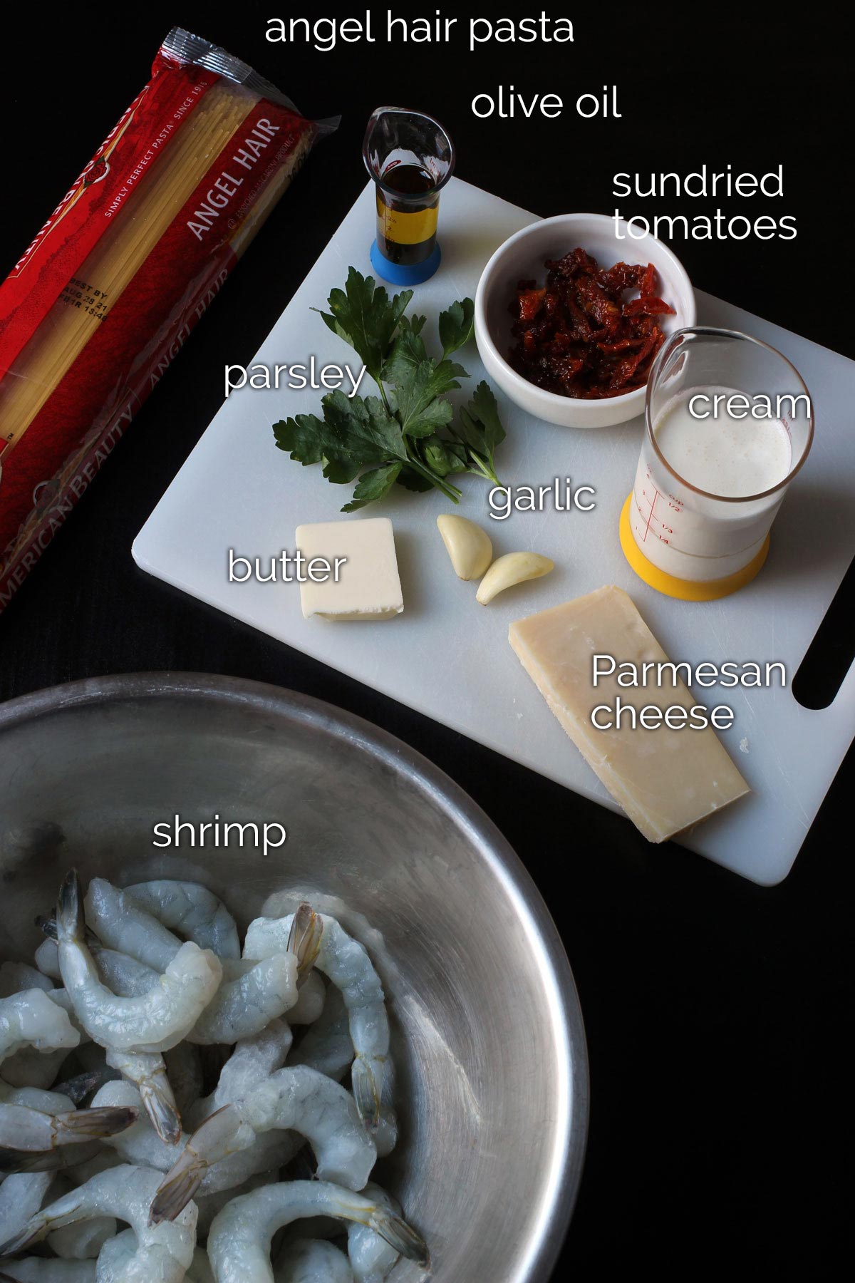 ingredients for shrimp pasta dish laid out on cutting board and on black table.