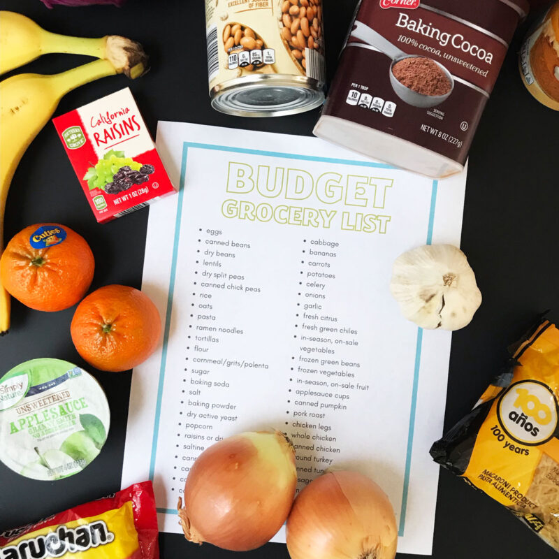 flatlay of printable budget grocery list with food items around on black table.