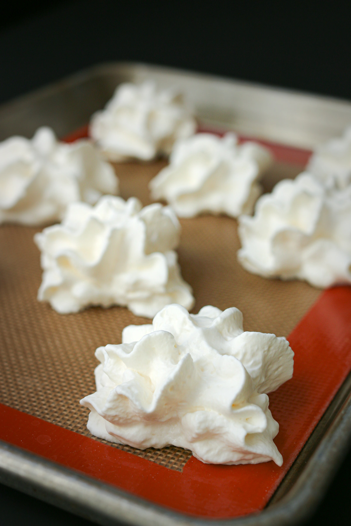 dollops of whipped cream in an array on a silicone mat in a baking sheet.