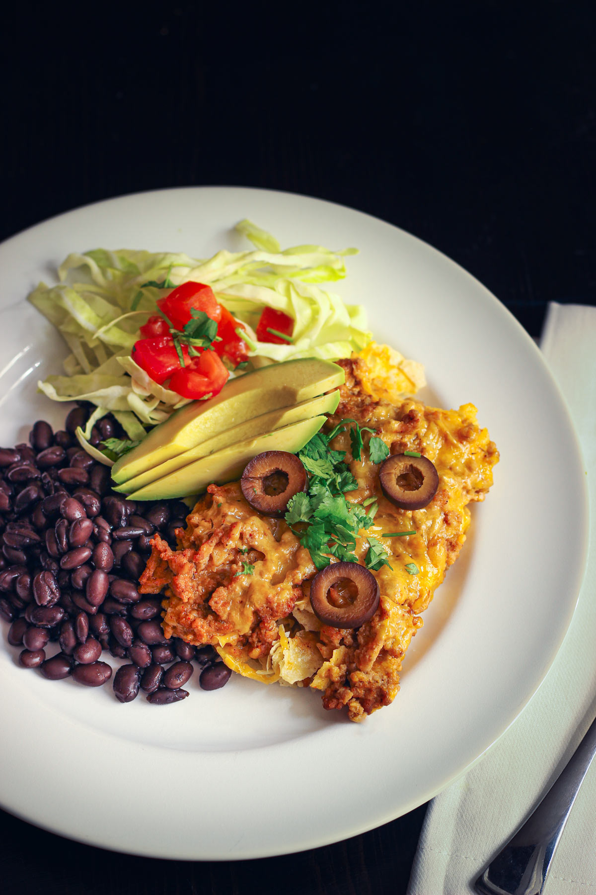 square of taco casserole on white dinner plate with beans and salad.
