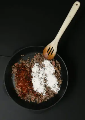 browned ground beef in skillet with taco seasoning and flour sprinkled over the top.