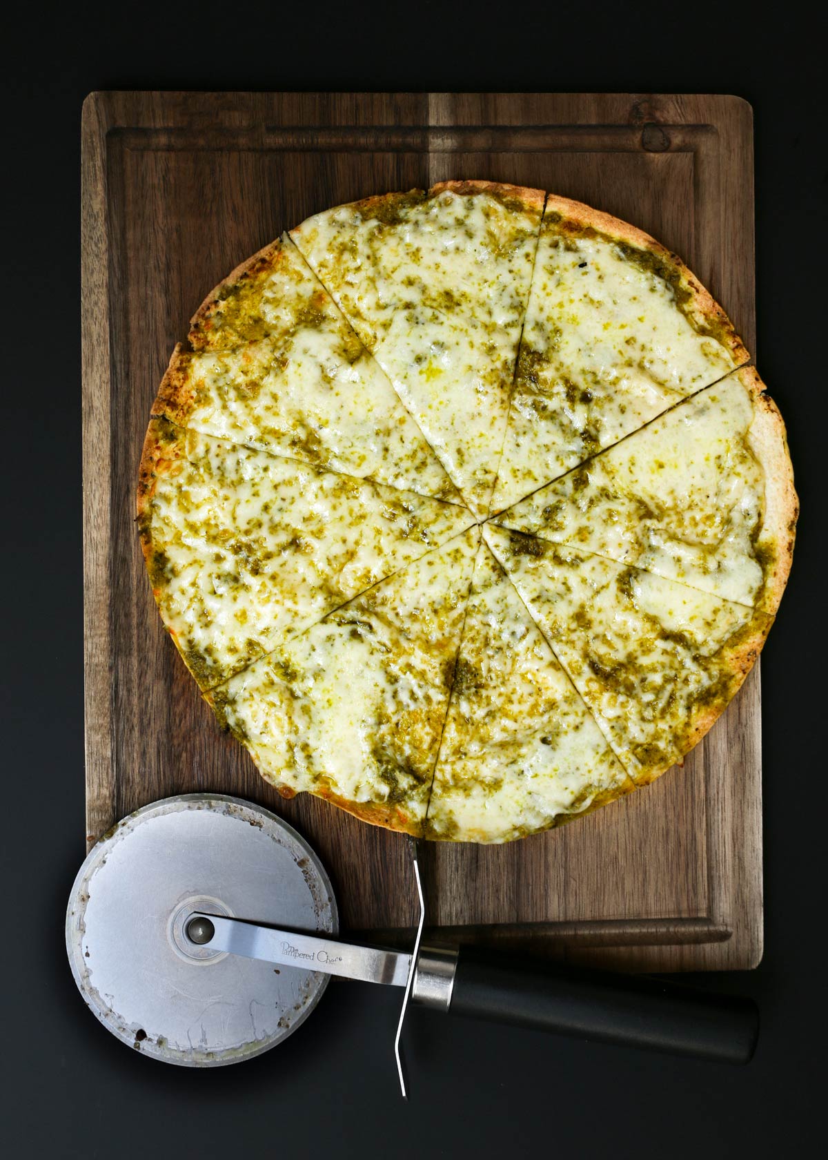 tortilla pizza with pesto on dark wood board sliced with pizza wheel on the board.