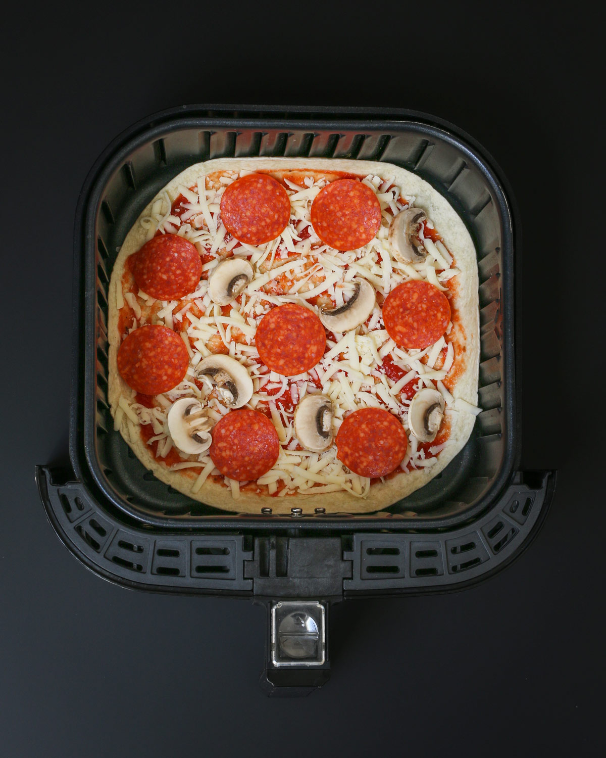tortilla with sauce, cheese, and toppings in air fryer basket.