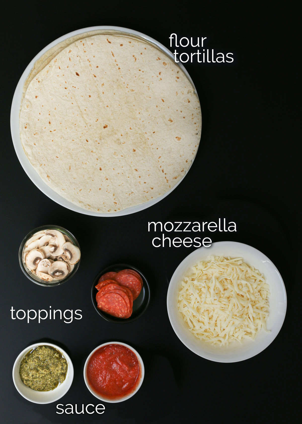 ingredients for tortilla pizza on black table.