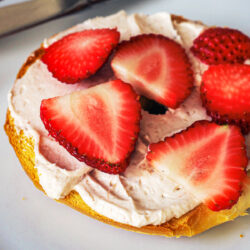 close-up of strawberries on cream cheese on bagel half.