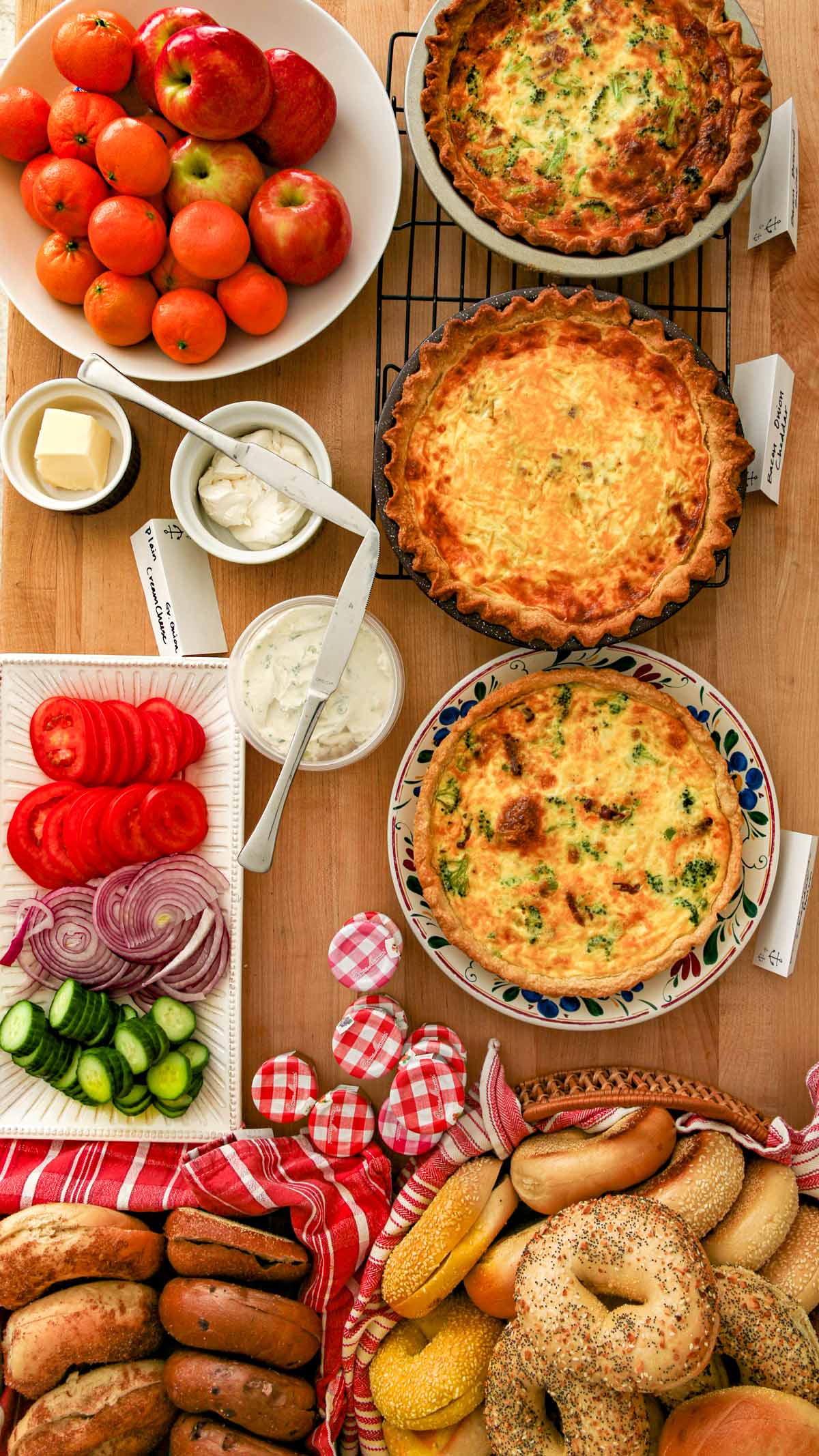 an array of quiche, bagels, and other brunch food items on a wood table.