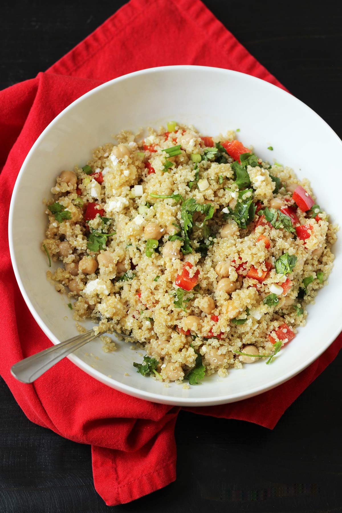 white bowl of quinoa salad on red cloth on black table.