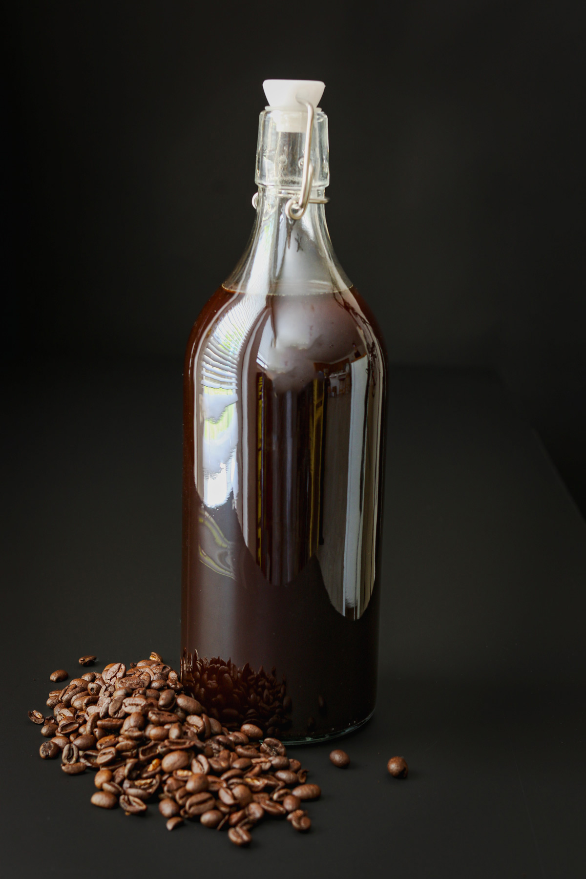 bottle of cold brew concentrate on black table with coffee beans at the base.