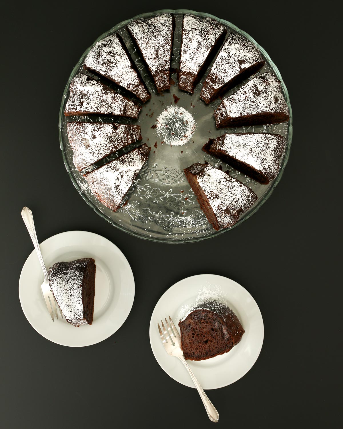 overhead shot of bundt cake on cake platter cut into slices and two plates with cake slices and forks.