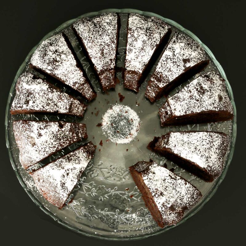 sliced chocolate zucchini bundt cake topped with powdered sugar on a glass cake stand.