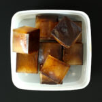 coffee ice cubes in white freezer box on black table.