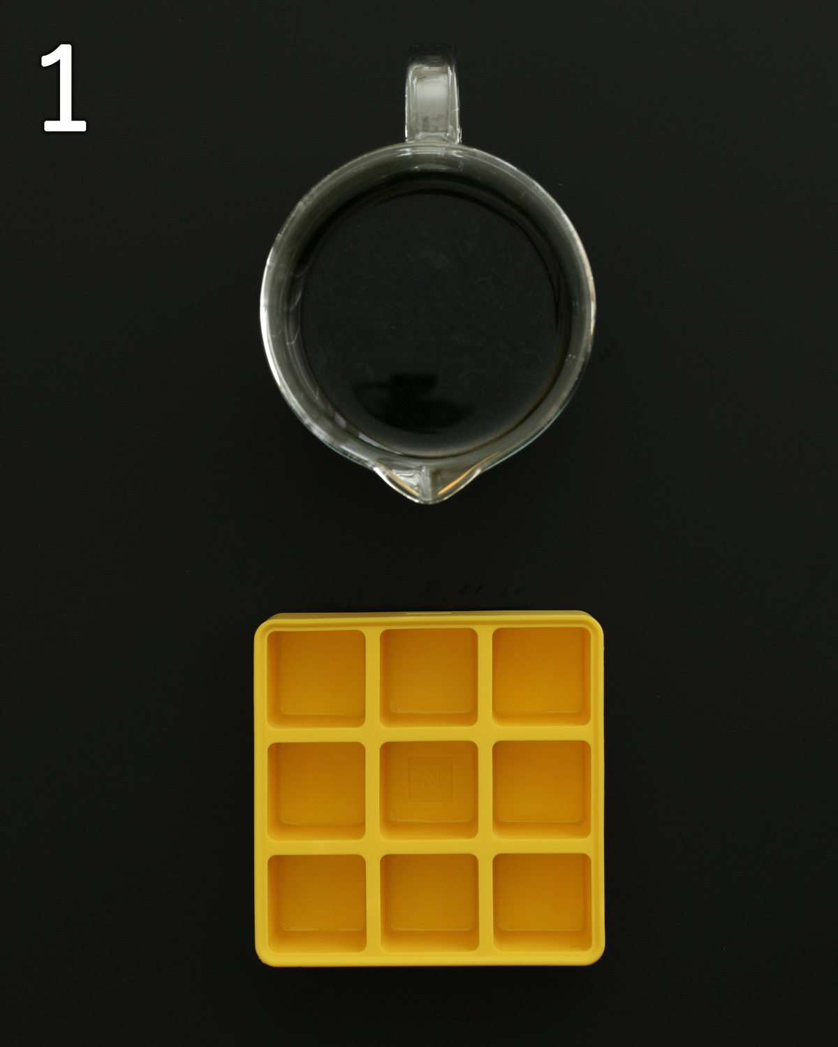 carafe of coffee next to yellow silicone ice cube tray on black table.