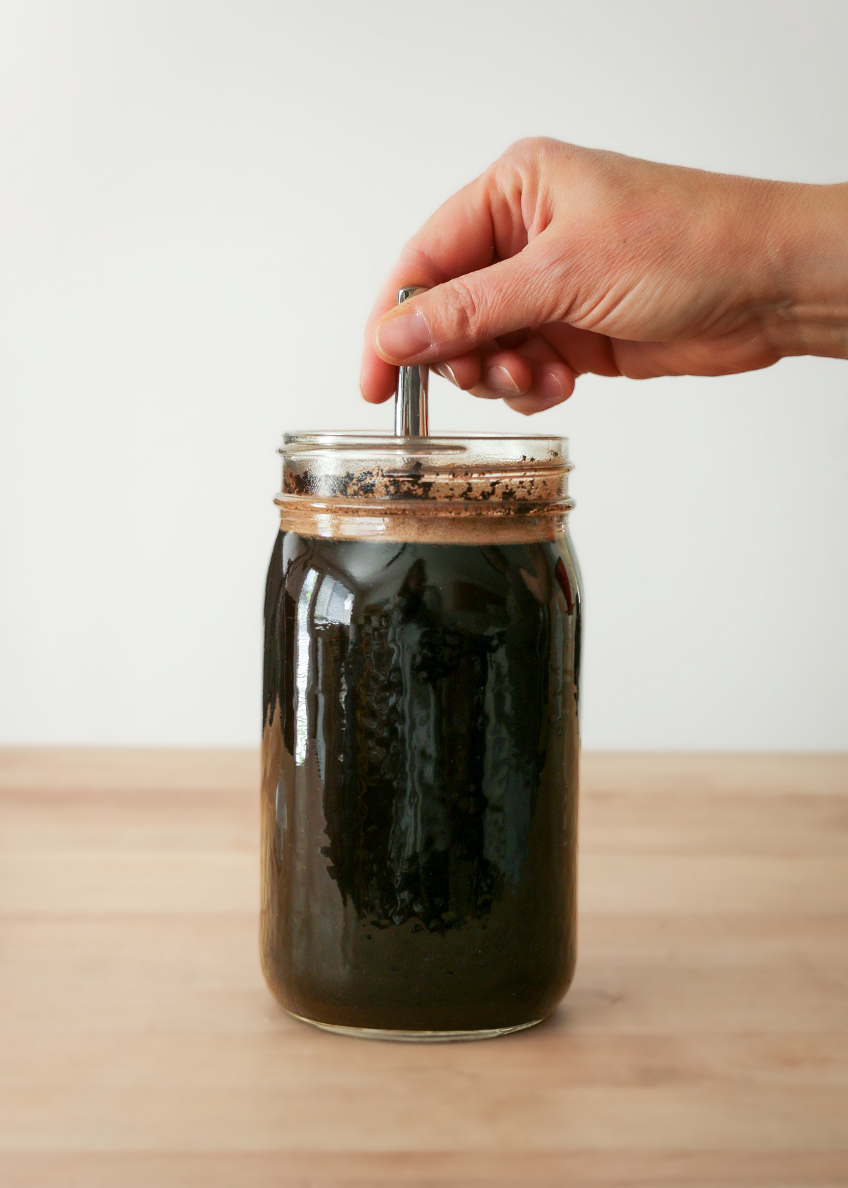 stirring the cold brew and coffee grounds in the jar.